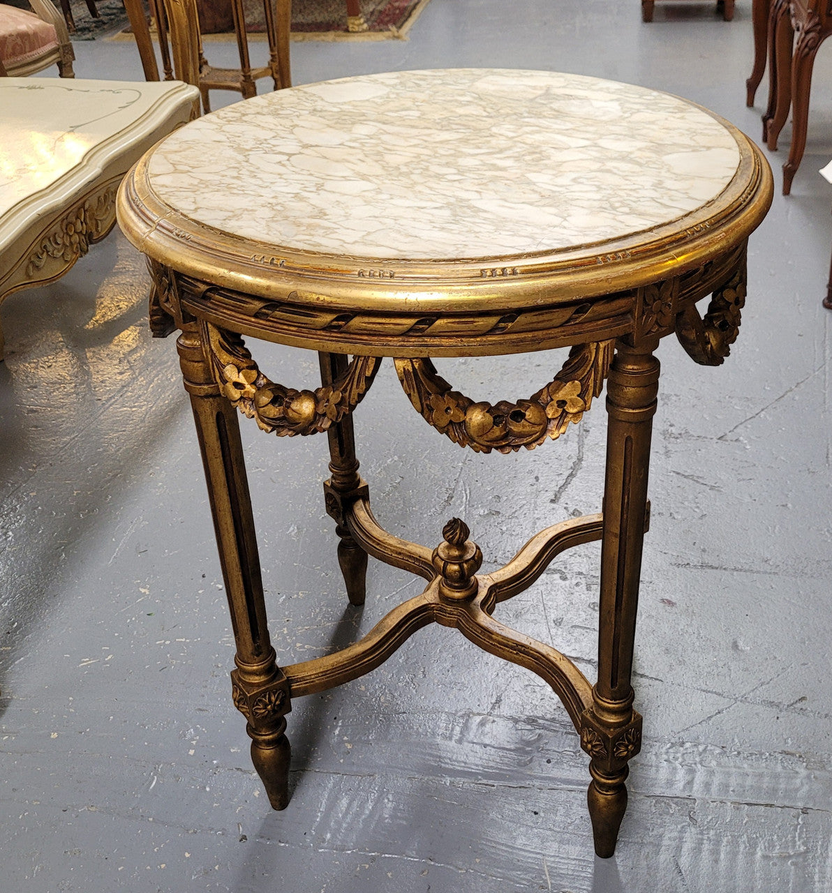 French Louis XVI style round marble topped gilded lamp/side table featuring lovely carved swags and undercarriage. It has been sourced from France and is in good original detailed condition.
