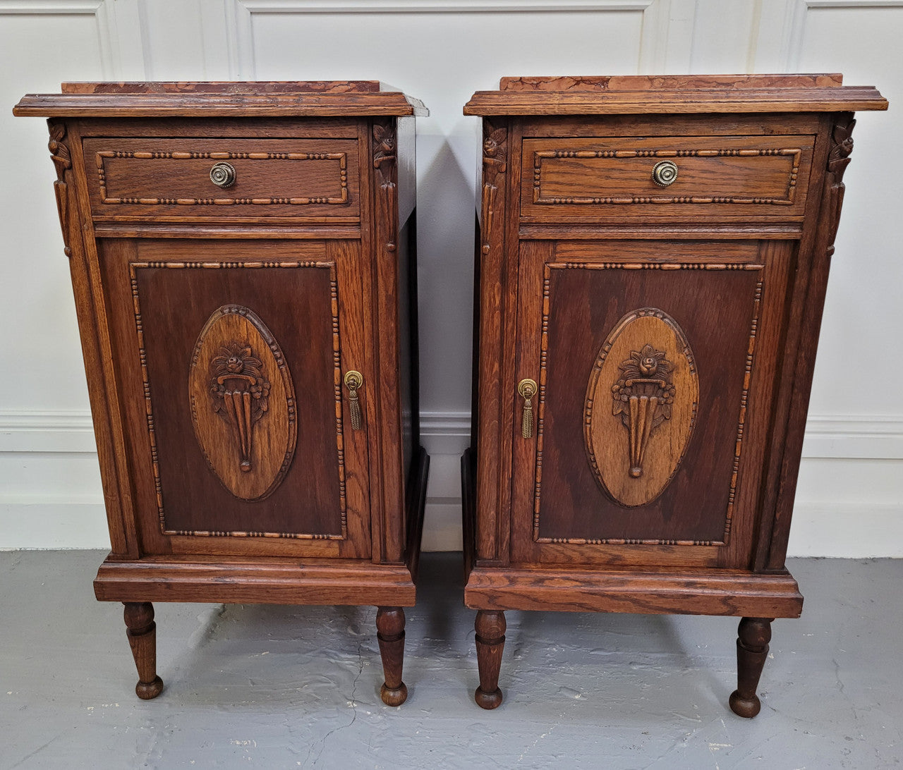 Pair of French Art Deco Oak and rouge inset marble top bedside cabinets. They have one drawer and one cupboard with elegant carving on the door. They have been sourced from France and are in good original detailed condition.