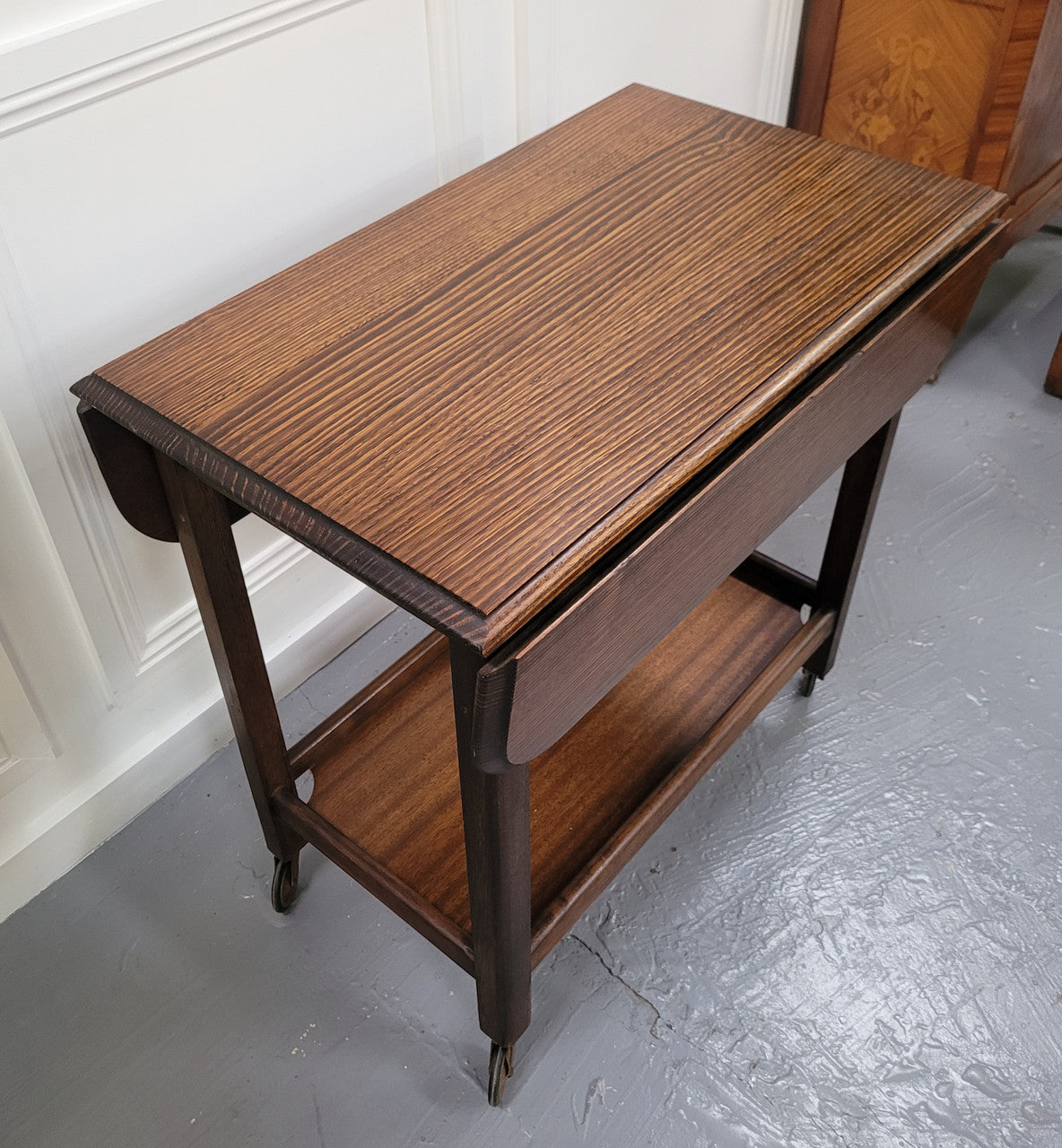 Oak drop leaf auto trolley on wheels. Both sides open up to make a larger table. It is in good original detailed condition.