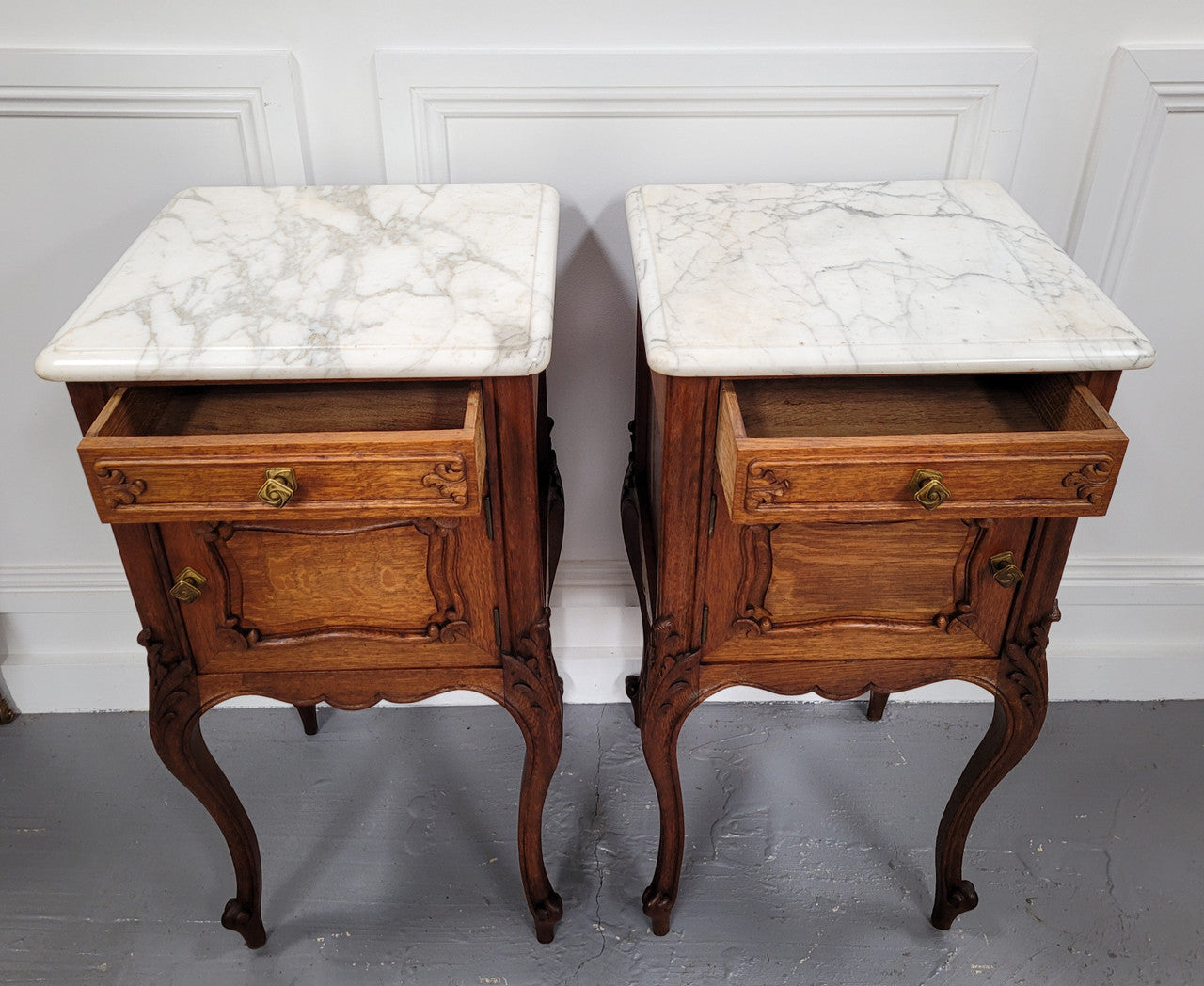 Pair of French Antique Louis XV style Oak marble top night stands. They have beautiful carved cabriole legs and beautiful white marble along with a drawer and cupboard for storage space. They have been sourced from France and are in good original detailed condition.