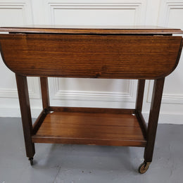 Oak drop leaf auto trolley on wheels. Both sides open up to make a larger table. It is in good original detailed condition.