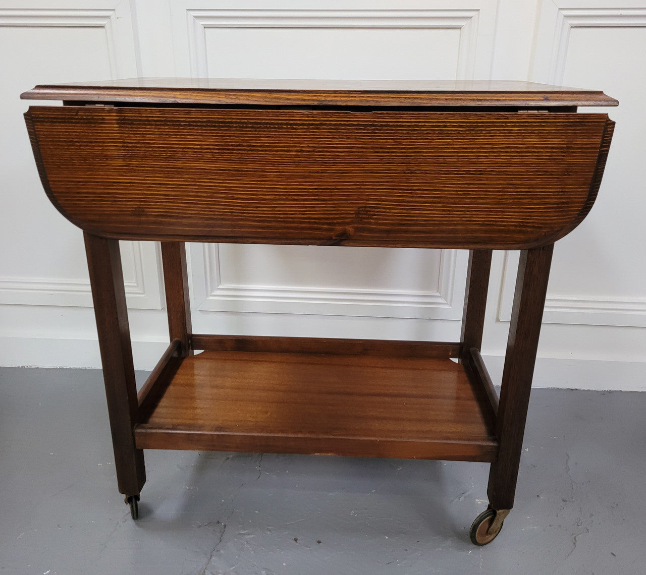 Oak drop leaf auto trolley on wheels. Both sides open up to make a larger table. It is in good original detailed condition.