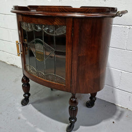 Oak Tudor auto trolley with beautiful leadlight glass. It is on wheels and the door open up to a cabinet with one shelf. In good original detailed condition.