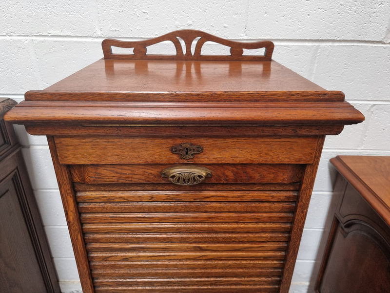 Antique Edwardian roll top Tambour file cabinet desk. This practical antique tambour front filing cabinet dates around 1900 in the Edwardian period and is constructed from Oak. This antique cabinet has an adjustable writing slope, above a tambour front with key and working lock. It has been sourced locally and is in good original detailed condition.