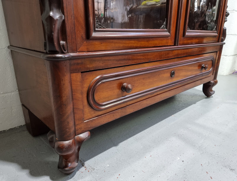 Antique Mahogany two door Biedermeier style bookcase with four fully adjustable shelves and a drawer at the bottom. The two wooden finials at the top are easily removed for a different look of desired. In good original detailed condition.