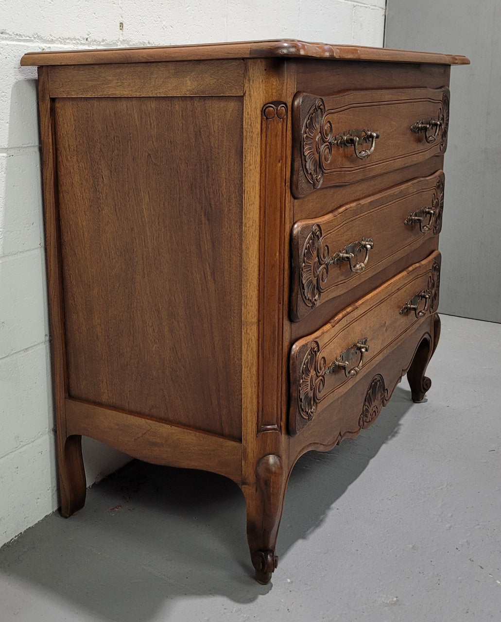 A French Walnut carved three drawer commode with lovely handles and in good original detailed condition.A French Walnut carved three drawer commode with lovely handles and in good original detailed condition.